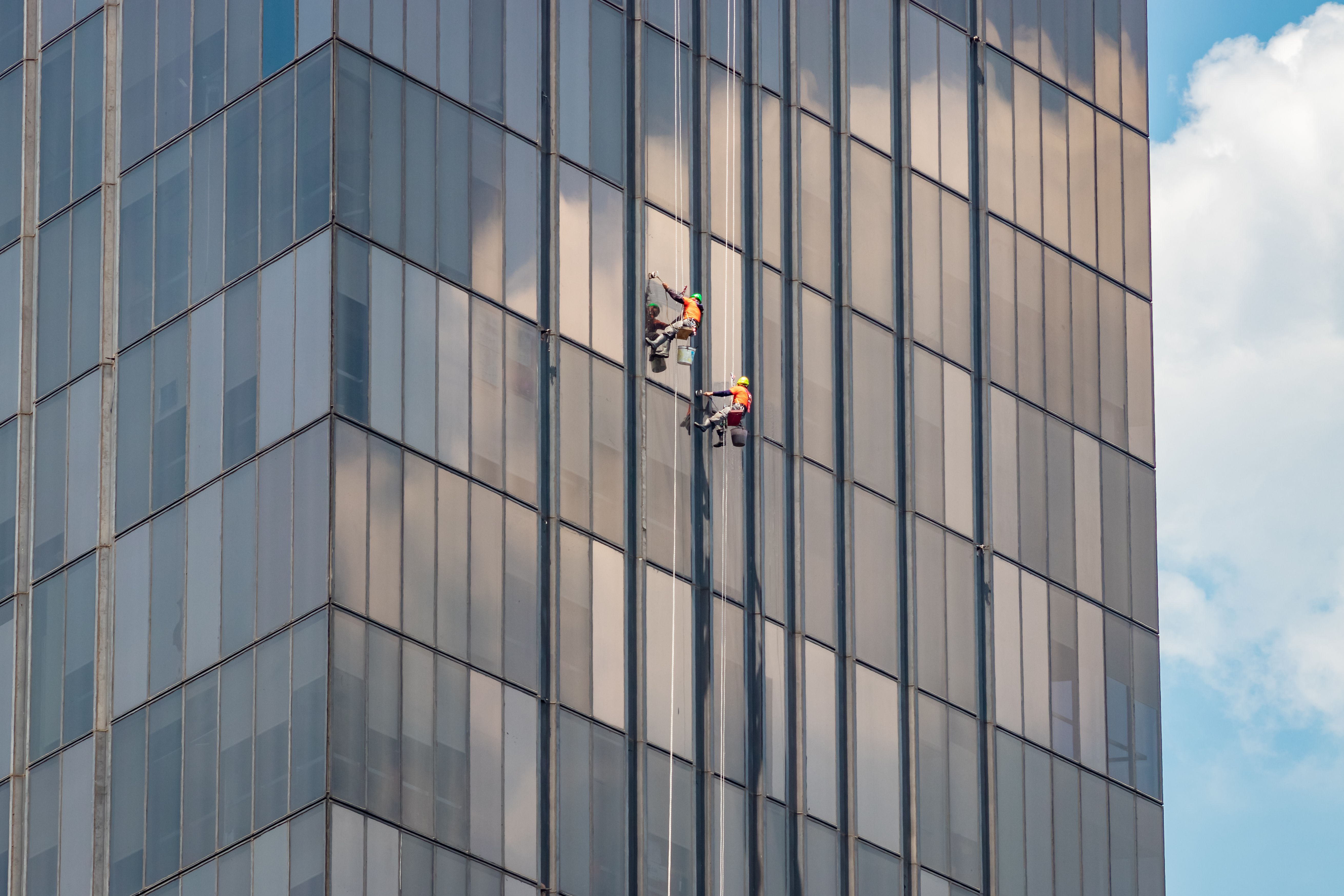 Schoonmakers aan het werk aan de gevel van een modern kantoorgebouw.